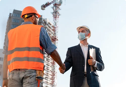 Two construction workers shaking hands at a building site