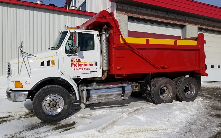Red-and-yellow dump truck parked in front of a building on a job site